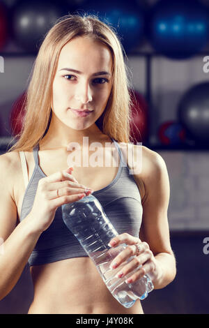 Young blonde girl standing with bottle of water in fitness center. Warm color toned image Stock Photo