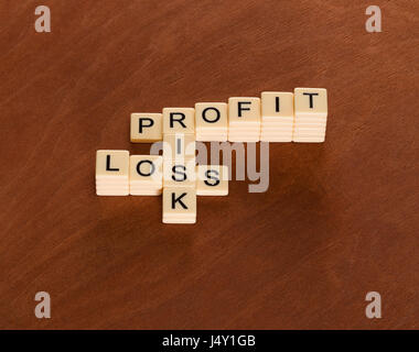 Crossword puzzle with words Risk, Profit and Loss. Risk management concept. Chart of ivory tiles with capital letters on mahogany board. Stock Photo