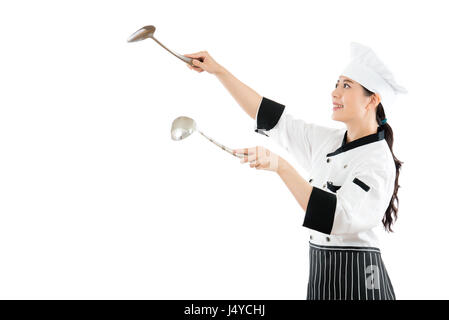 mixed race asian chinese model playing as a chef holding a spatula and spoon of silver tools on a white background performing cooking seriously watchi Stock Photo