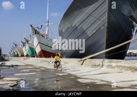 Man on bicycle with reflections and pinisi, Sunda Kelapa Harbour, Jakarta, Indonesia Stock Photo