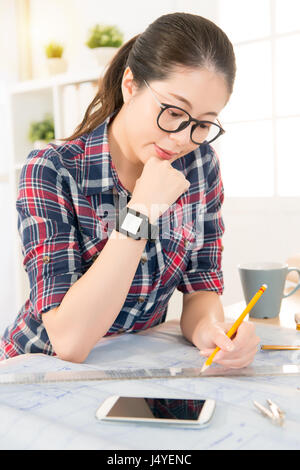 profession and job occupation concept. Young asian architect woman wearing smartwatch and smartphone put on table sketch work for new design while at  Stock Photo