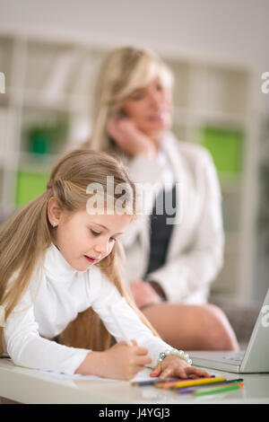 Cute girl doing homework while mother working at home Stock Photo