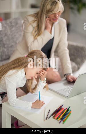 Woman using telephone in home office with laptop while young girl drawing Stock Photo