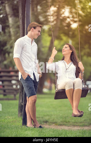 romantic couple  having fun in park girl on swing Stock Photo
