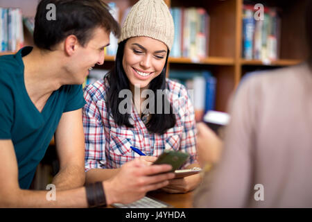 Couple of beautiful young classmates having fun on cell phone after class Stock Photo