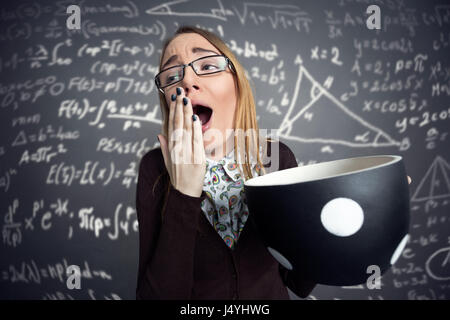 tired female student yawning with big cup of coffee Stock Photo