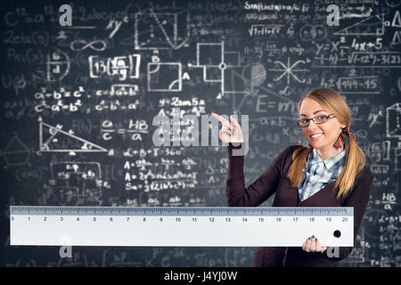 female smiling student with a big ruler pointing formulas on background Stock Photo