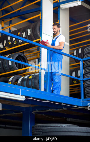 mechanic in blue uniform checking a stack of tires while holding a clipboard Stock Photo
