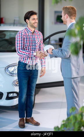 Seller or car salesman and customer in dealership, they shaking hands and seal the purchase of the auto or new car. Stock Photo