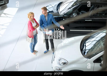 Friendly car dealer showing young women new car in showroom Stock Photo