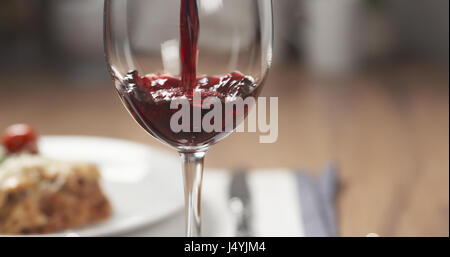 pouring red wine in glass with lasagna at background Stock Photo