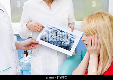 Closeup portrait worried scared female patient, woman siting in chair medical office, looking at panoramic dental x-ray image listening to doctor givi Stock Photo