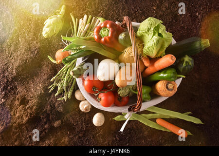 Assortment of vegetables in a wicker basket on soil. Horizontal composition. Top view Stock Photo