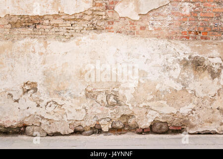 Old weathered vintage brick wall with broken plaster and pavement on the ground. Grungy urban background. Stock Photo
