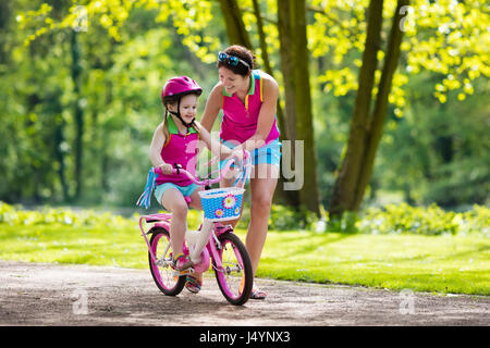 Child riding bike. Kid on bicycle in sunny park. Mother teaching little girl to cycle. Preschooler learning to balance wearing safe helmet. Sport for  Stock Photo