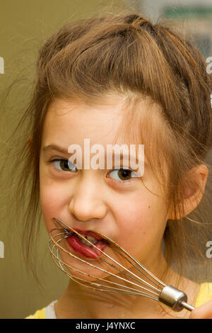 Little girl licking chocolate off the mixer beater after mixing dough for birthday cake. Permissive parenting, learning through experience, child inclusion, homemade food concept. Stock Photo