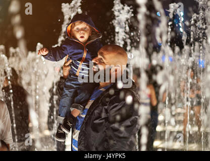 Father hold boy kid in water fountain park. Happy father with small kid Stock Photo