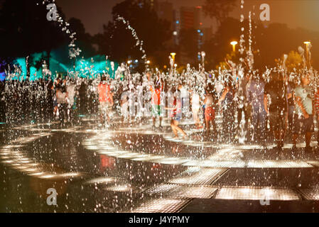 Water fountain splashes at night on blur playing people background Stock Photo