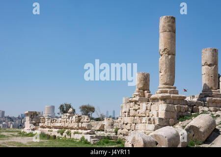 Ancient Roman ruins of Temple of Hercules at Amman Citadel with view of Amman city and Jordanian flag in the background. Fallen blocks are in front. Stock Photo