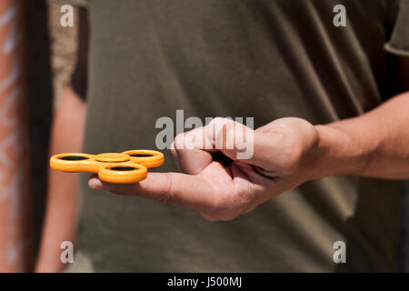 closeup of a young caucasian man playing with a yellow fidget spinner in the street Stock Photo