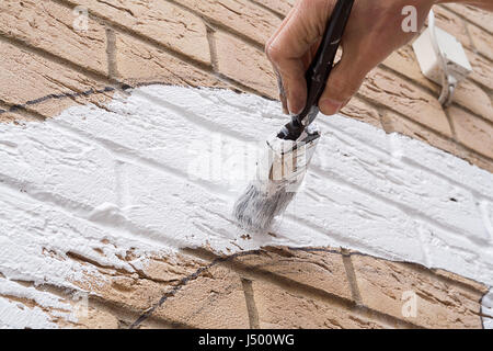 Painting  with a  brush on a brick wall the undercoat  for an art design  Design is scetched first and white paint filled in before  final colour coat Stock Photo