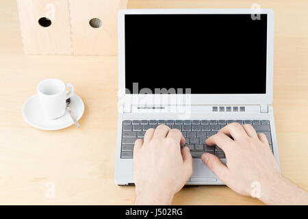 Business man working on laptop on brown wooden workplace table with cup and folders - blank screen as copy space Stock Photo