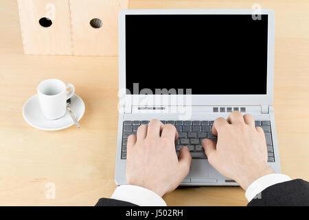 Business man working on laptop on brown wooden workplace table with cup and folders - blank screen as copy space Stock Photo