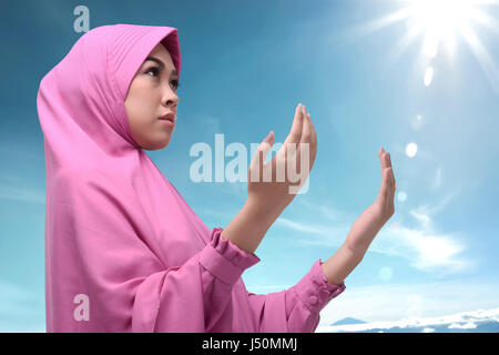 Young asian muslim woman in hijab dress praying against blue sky background Stock Photo