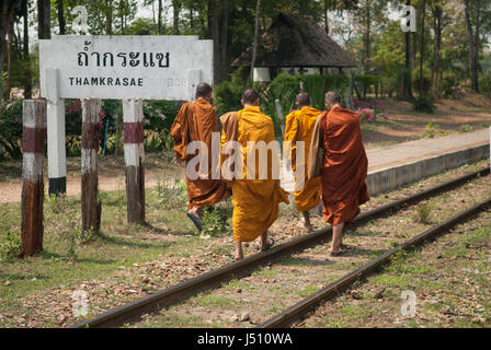 Four buddhist monks walking along the railway track at Thamkrasae Bridge station, Thailand Stock Photo