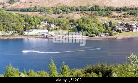 A speed boat makes waves in Loch Long, a sea loch in the West Highlands of Scotland, with Arrochar village behind. Stock Photo