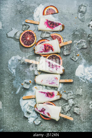 Healthy summer dessert. Blood orange, yogurt and granola popsicles on ice cubes over grey concrete background, top view, vertical composition. Clean e Stock Photo