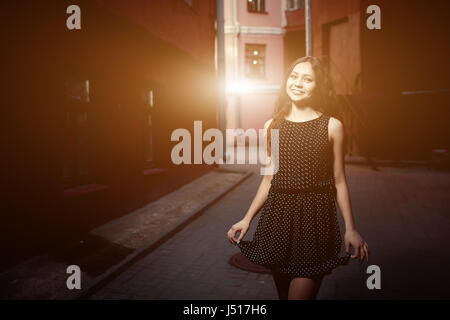 Beautiful brunette young woman wearing dress and walking on the street. Flare for text and design. Lifestyle in the city. Stock Photo