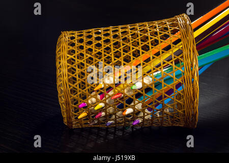 Sharp tips of colored pencils sharpen from sections of a wicker tube, on a dark wooden background Stock Photo