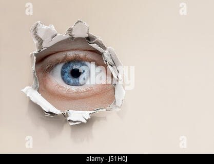 eye looking through hole in wall Stock Photo