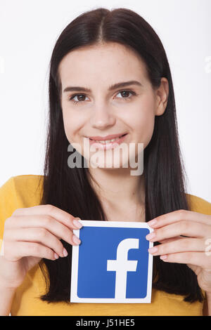 KIEV, UKRAINE - August 22, 2016: Woman hands holding facebook icon sign printed on paper on white background. Facebook is well-known social networking service. Stock Photo