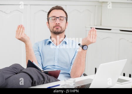 Businessman meditating in the office with his legs on the desk Stock Photo