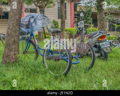 Luodong, Taiwan - October 18, 2016: A three-wheeled bicycle with a rusty luggage basket leaned against a tree. Stock Photo