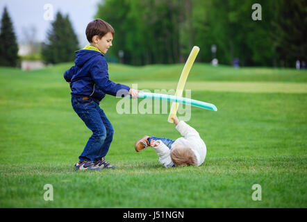 Preschool boys fighting with toy swords in park Stock Photo