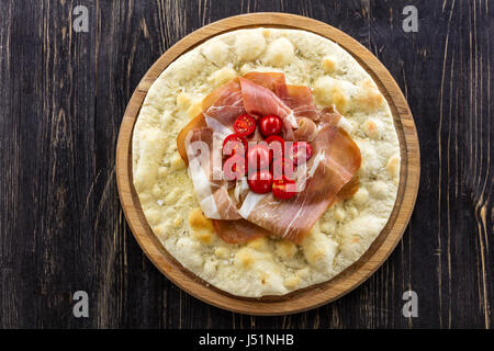 Focaccia with prosciutto and cherry tomatoes over wooden background Stock Photo