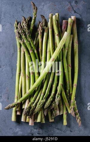 Bundle of young raw uncooked organic green asparagus over gray blue metal texture background. Top view. Healthy eating Stock Photo