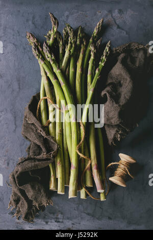 Bundle of young raw uncooked organic green asparagus on sackcloth rag over gray blue metal texture background. Top view. Healthy eating. Toned image Stock Photo