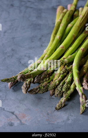 Bundle of young raw uncooked organic green asparagus over gray blue metal texture background. Close up. Healthy eating Stock Photo