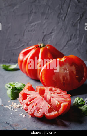 Whole and sliced organic tomatoes Coeur De Boeuf. Beefsteak tomato with pink salt and basil on blue gray metal texture background. Close up with space Stock Photo
