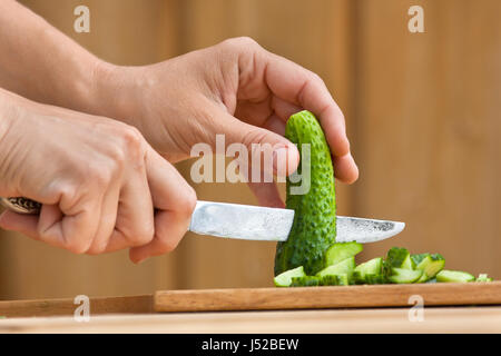hands cutting fresh cucumber on the wooden chopping board Stock Photo