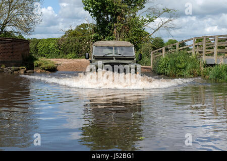 Model released image of a man driving a 1973 ex army Land Rover Series 3 Long Wheel Base into the river VER which forms a ford at Redbournbury, Herts. Stock Photo