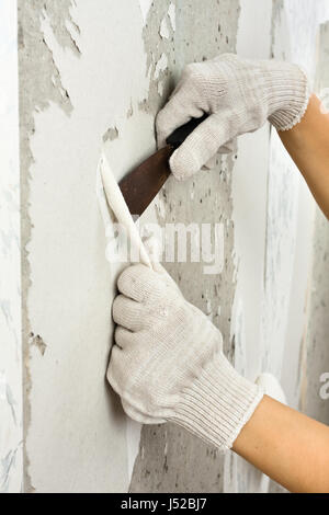 hands removing wallpaper from wall with spatula Stock Photo