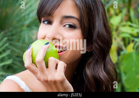 young woman eating an apple on a green leafy background Stock Photo