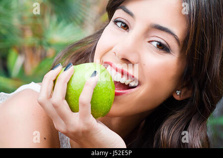 young woman eating an apple on a green leafy background Stock Photo