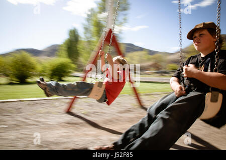 Two boys swinging on a swing set at a park in rural Utah. Stock Photo