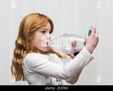 A seven year old girl using a Ventolin inhaler with a volumatic spacer device for asthma relief. Stock Photo